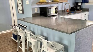 A modern kitchen with a central island, bar stools, a microwave, a coffee maker, and pendant lights. - The Mark at Surfside, Apt. 5 (Surfside Beach)