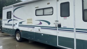 Een witte camper met de naam 'MIRADA' op de zijkant, een schuifdeur en een raam met een waarschuwingsbord.