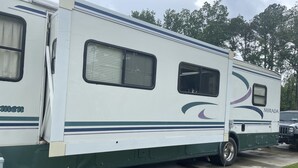 Een witte camper met groene accenten en een logo, geparkeerd op een betonnen oppervlak.
