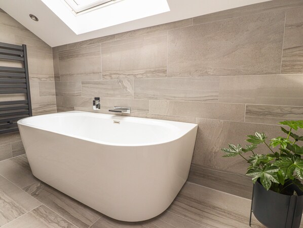 A modern bathroom with a freestanding bathtub, tiled walls, and a skylight. - Laundry Cottage (Milnthorpe)