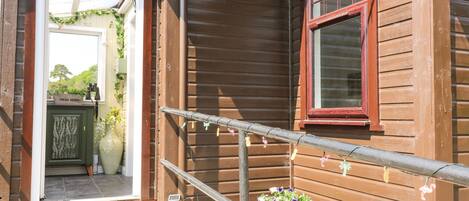 A wooden house with a red window, a door leading to a covered porch, and potted plants outside.
