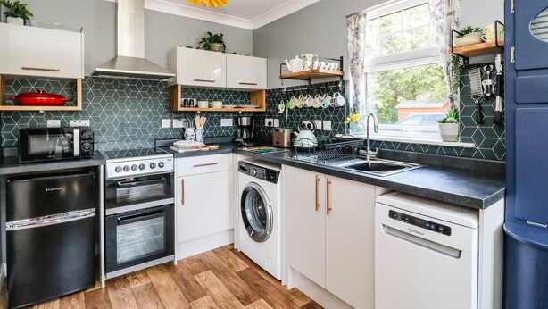 A compact kitchen with white cabinets, a microwave, stove, oven, washing machine, and a dishwasher. - Kilmartin View (Lochgilphead)