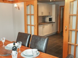 A dining area with a wooden table set for two, a bottle of wine, and two wine glasses. There are white cabinets and a microwave in the background.