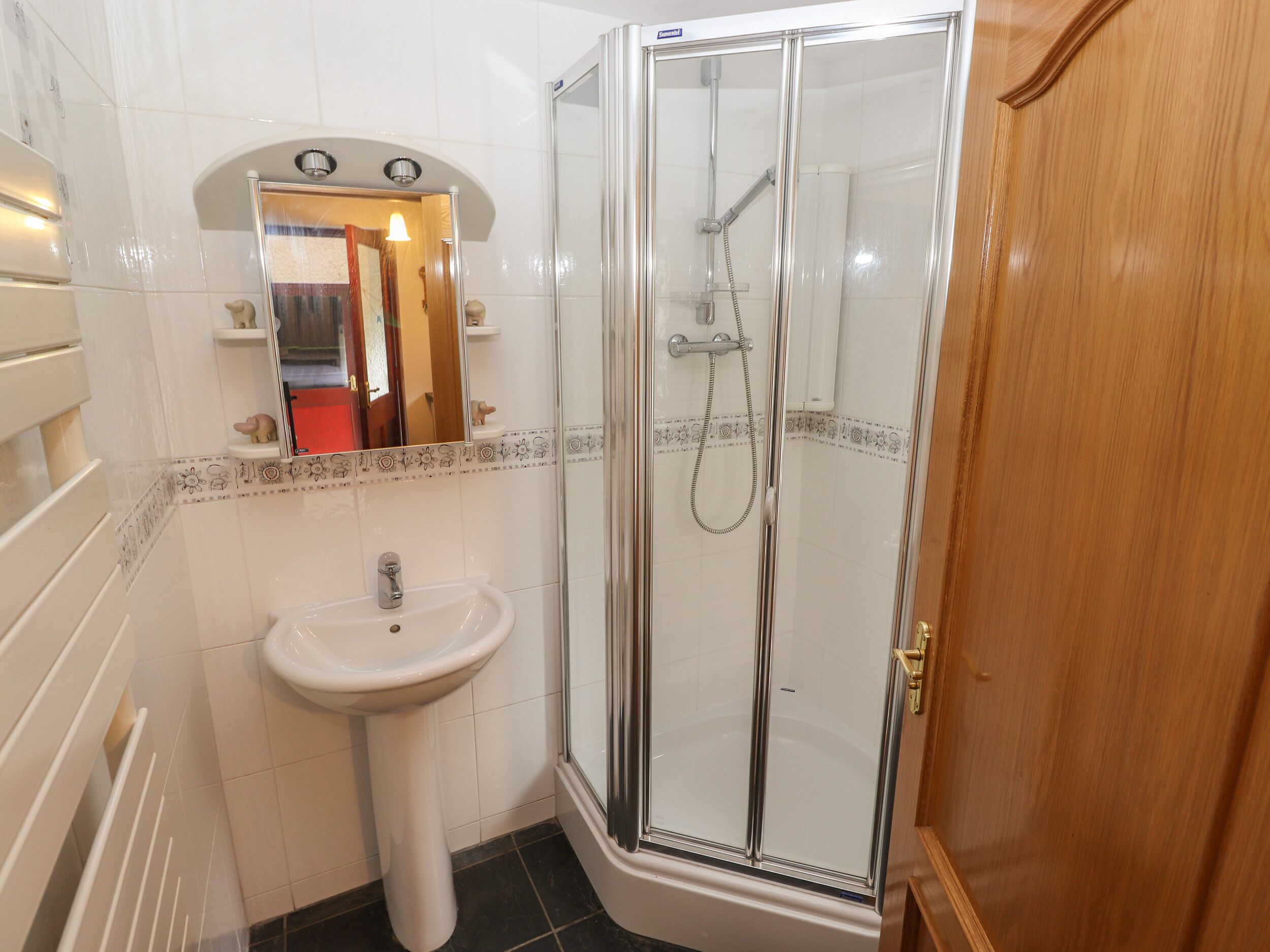 Un bany amb dutxa amb envàs de vidre, un lavabo de pedestal i un mirall sobre el lavabo.
