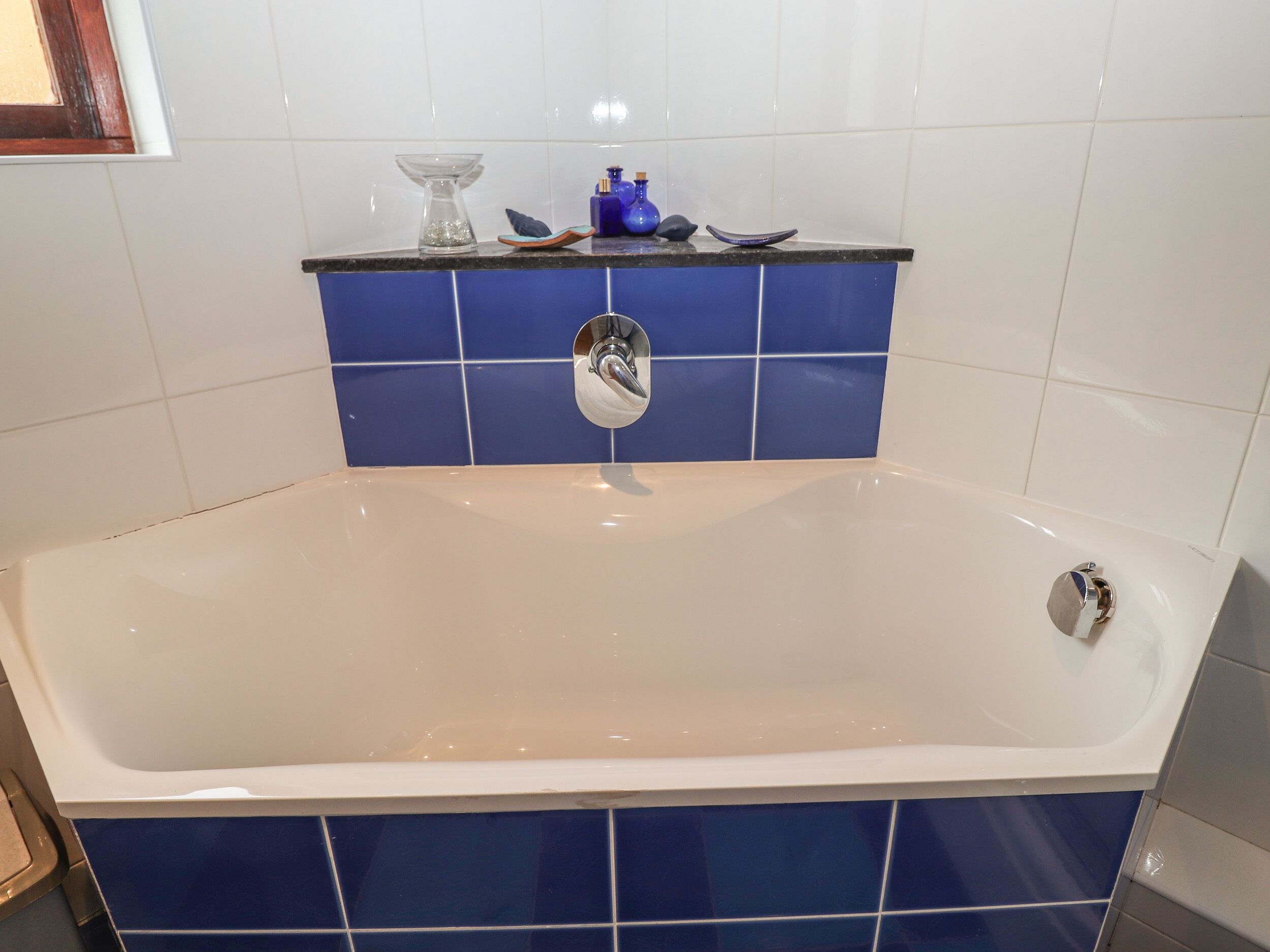 A bathroom with a bathtub, blue tiles, a white sink, and a blue soap dispenser.