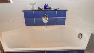 A bathroom with a bathtub, blue tiles, a white sink, and a blue soap dispenser.