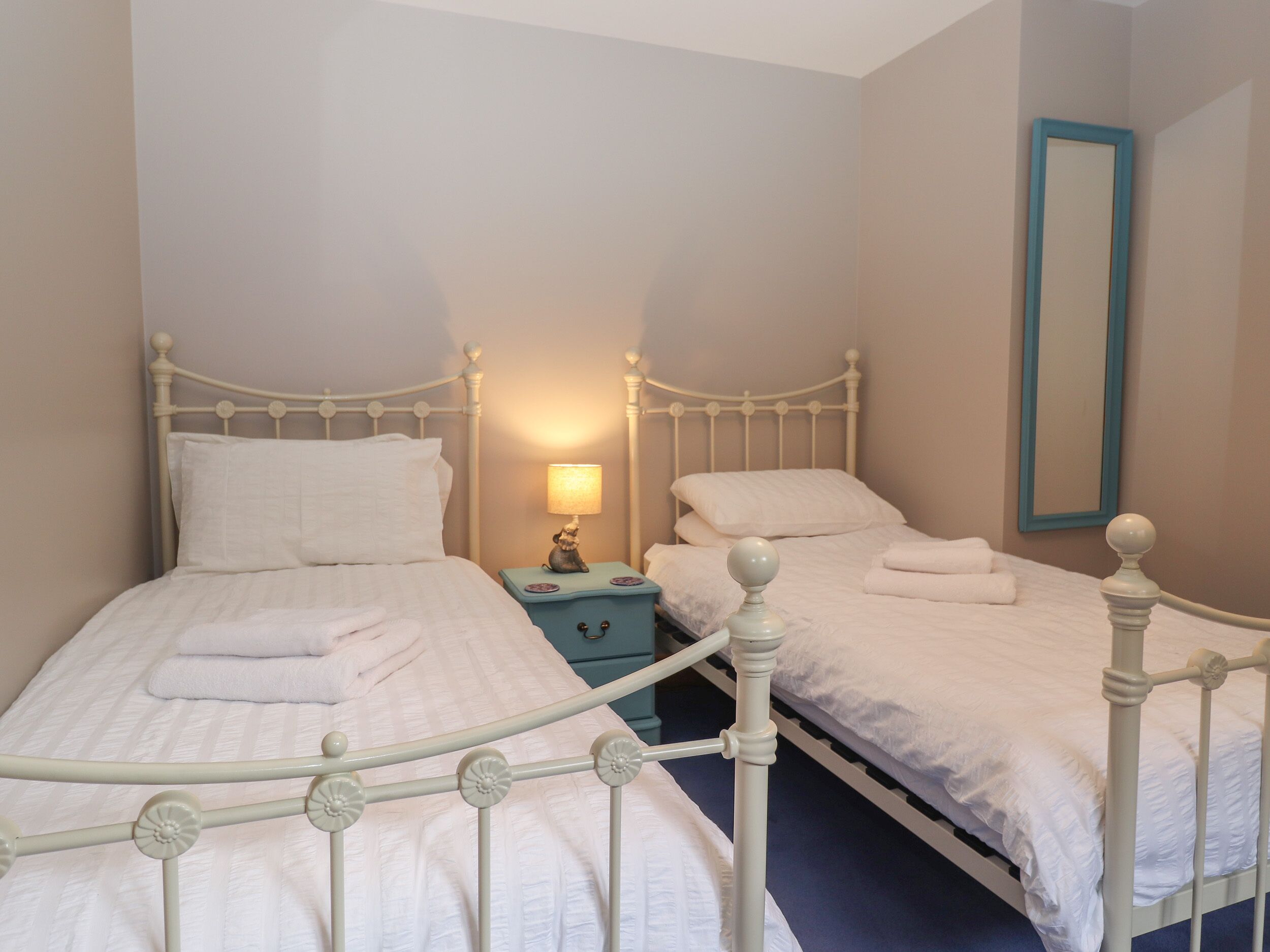A twin bedroom with two beds, a nightstand, a lamp, and a mirror.
