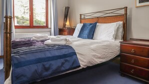 Una cama bien tendida con ropa de cama blanca y azul, un cabecero de madera y una mesita de noche con una lámpara.