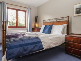 A neatly made bed with white and blue bedding, a wooden headboard, and a nightstand with a lamp.
