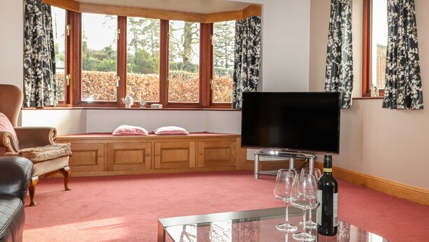 Una sala de estar con un sofá, una mesa de centro de vidrio, un televisor y una ventana con cortinas.