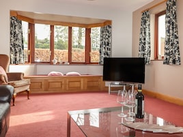 A living room with a sofa, a glass coffee table, a television, and a window with curtains.
