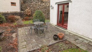Un patio con una mesa y sillas de piedra, una planta en maceta y un muro de piedra.