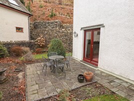 A patio with a stone table and chairs, a potted plant, and a stone wall.