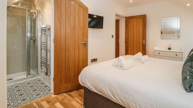 Ein Schlafzimmer mit einem großen Bett, einem Holzschrank, einem an der Wand montierten Fernseher und einem Duschbereich mit Glastür.