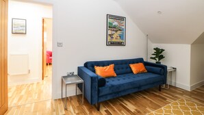 Ein modernes Wohnzimmer mit einem blauen Sofa, Holzboden, einem kleinen Beistelltisch und einem gerahmten Poster an der Wand.
