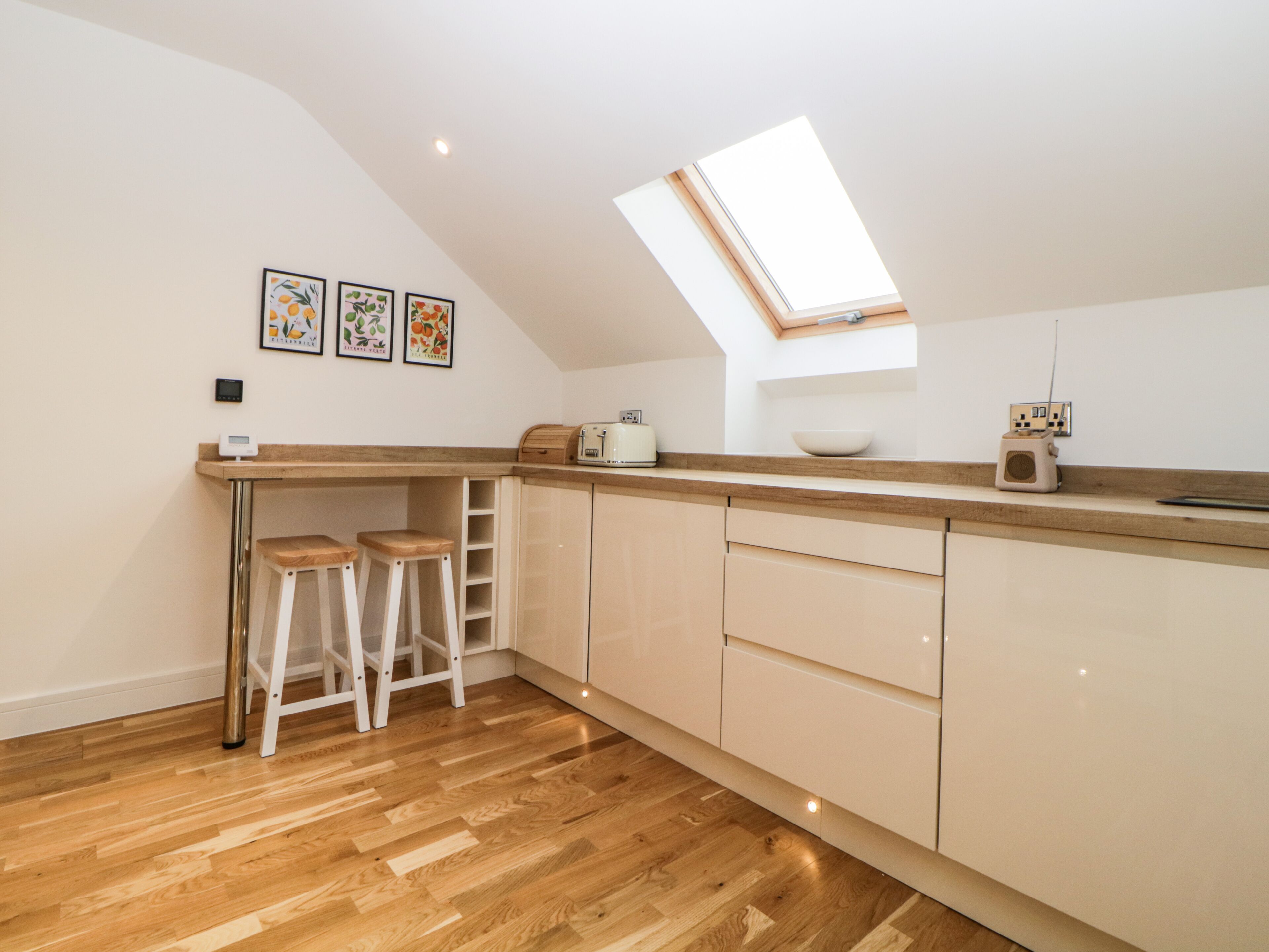 Une cuisine moderne avec un plancher en bois, une lucarne et un comptoir avec des tabourets.