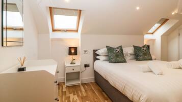 A bedroom with a bed, a nightstand, a lamp, a mirror, and a skylight.