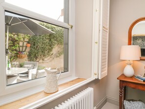 A room with a window overlooking a garden, a white radiator below, and a small table with a lamp and books.