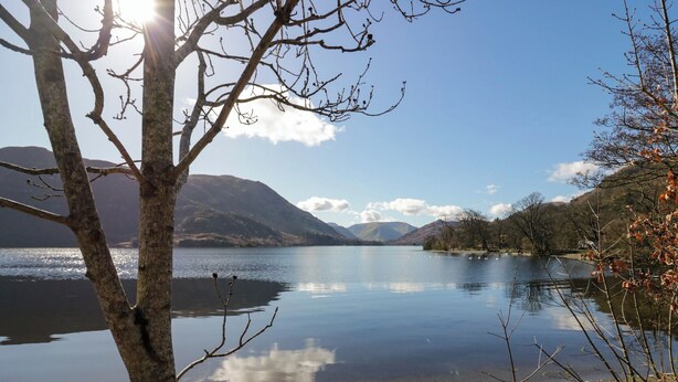A tranquil lake with clear reflections, surrounded by mountains and trees.