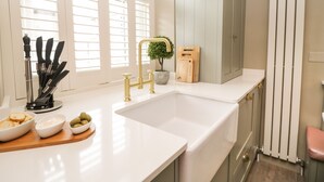 A kitchen with a white countertop, a gold faucet, and a wooden cutting board with a knife set.