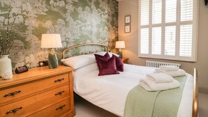 A bedroom with a bed, two bedside tables with lamps, a wooden dresser, and a window with blinds.