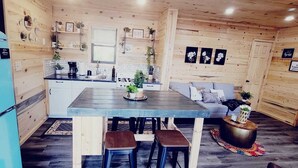 Une cuisine compacte avec un réfrigérateur bleu, des placards en bois, une table à manger avec des tabourets et un petit coin salon avec un canapé.