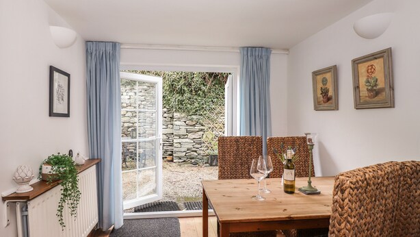 A dining area with a wooden table, two chairs, a bottle of wine, and a glass.