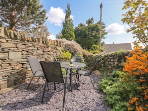 A stone wall, outdoor table with chairs, and a potted plant.