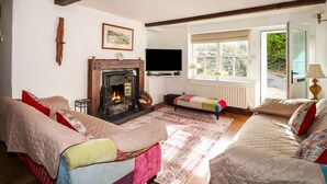 A cozy living room with a fireplace, sofas, a television, and a window with a view of greenery.