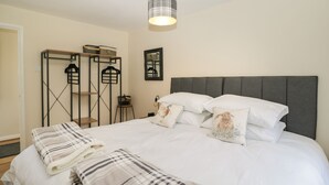 A neatly made bed with white bedding and striped pillows, a grey upholstered headboard, and a pendant light above. - Orchard House Cottage (Malmesbury)