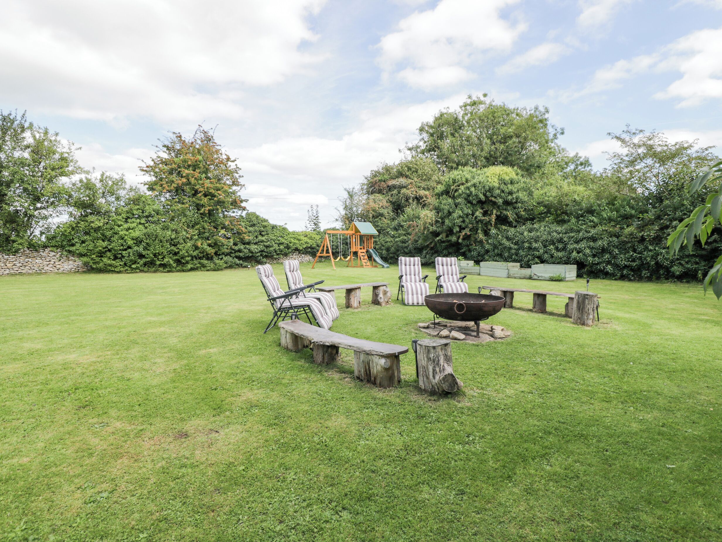 A backyard with a grassy lawn, a wooden fire pit, and striped chairs.