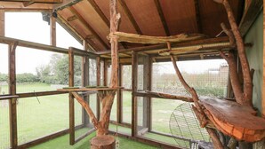 A bird enclosure with wooden perches and a mesh fence, surrounded by a grassy area. - Orchard House Cottage (Malmesbury)