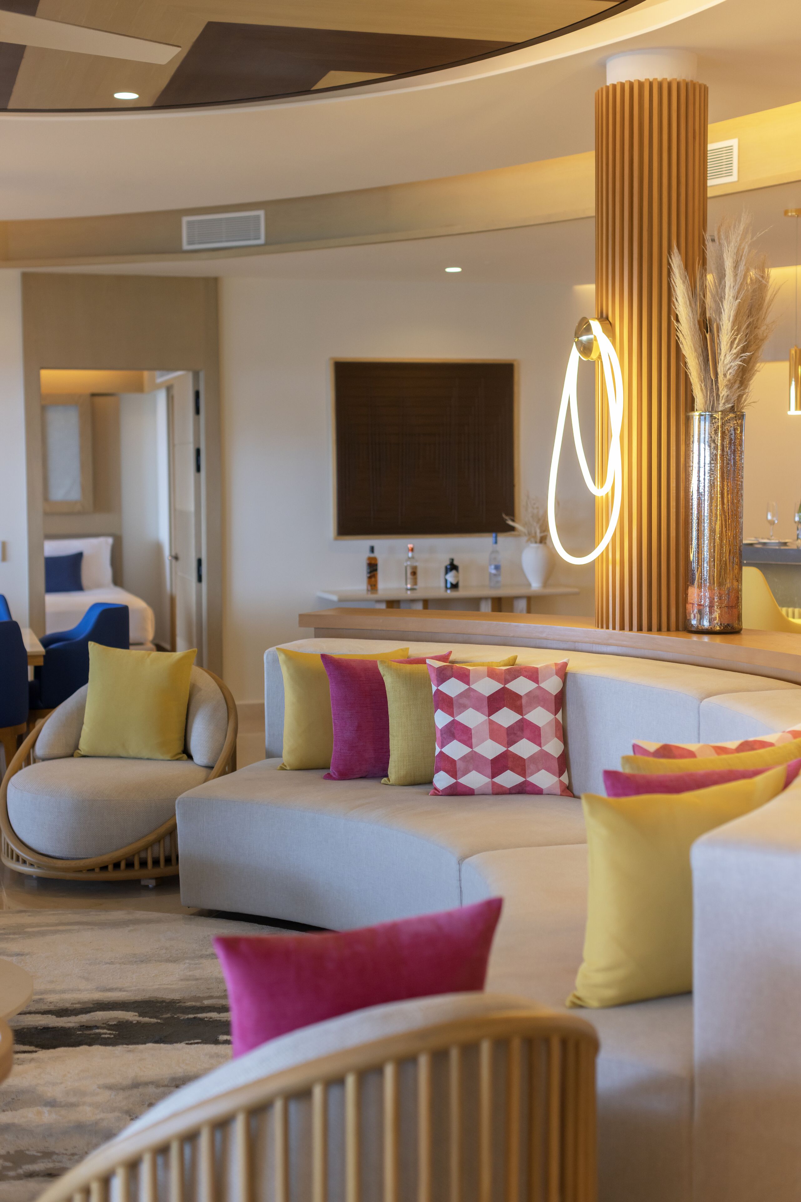 A modern hotel room with a curved sofa, a wooden column, and a decorative vase.