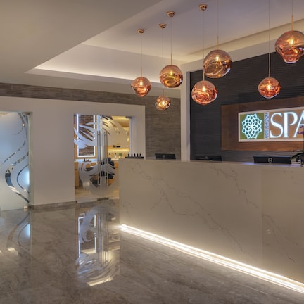 A modern spa reception area with a marble counter, hanging spherical pendant lights, and a visible staircase leading to the upper floors.