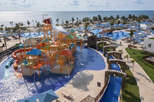 Un parque acuático con toboganes y piscinas, rodeado de palmeras y sombrillas de playa.
