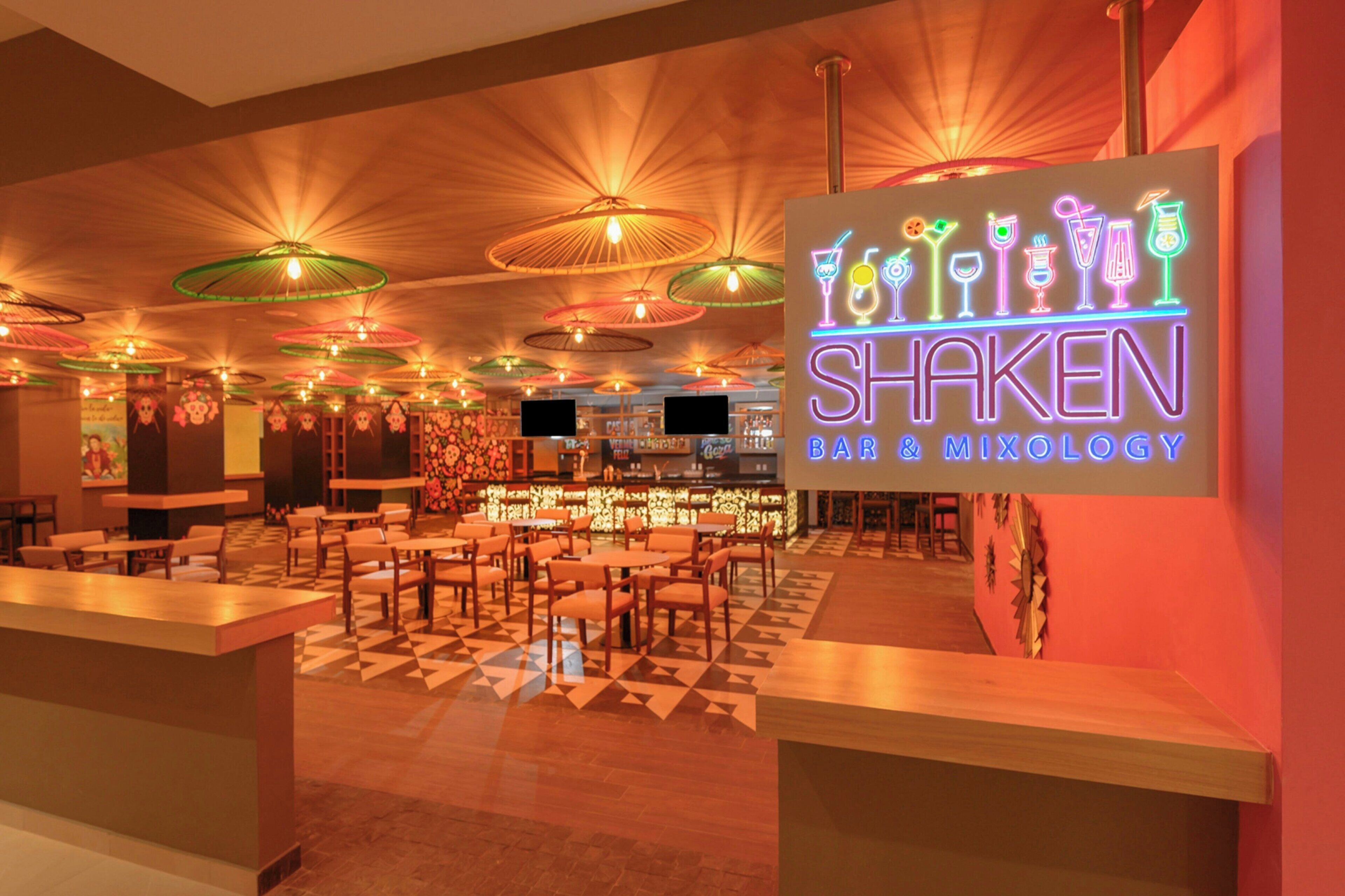 Zona de bar con un letrero de neón que dice 'SHAKEN BAR & MYOLOGY'.