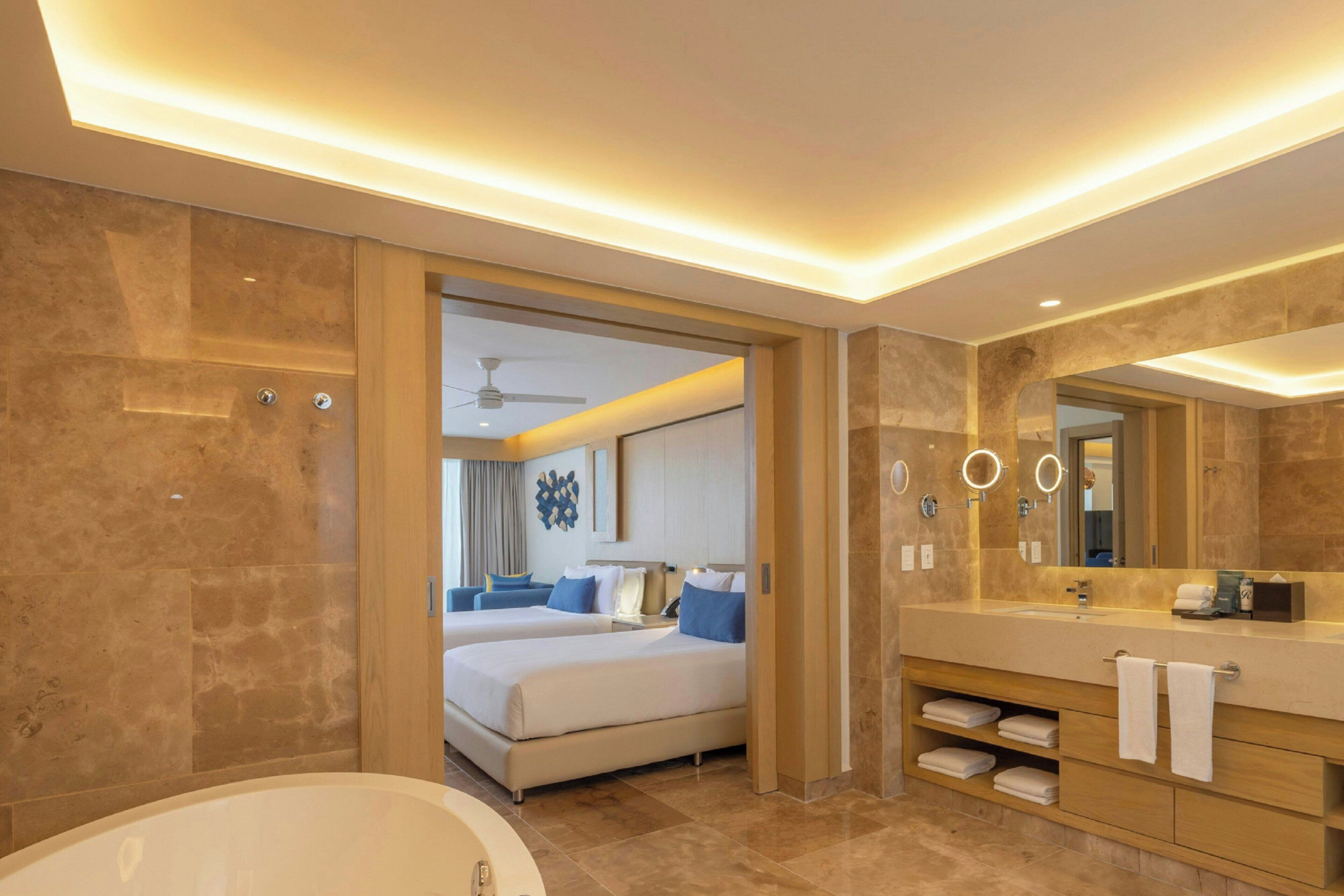 Un baño de hotel moderno con una bañera grande, una cama doble y un tocador con espejo.