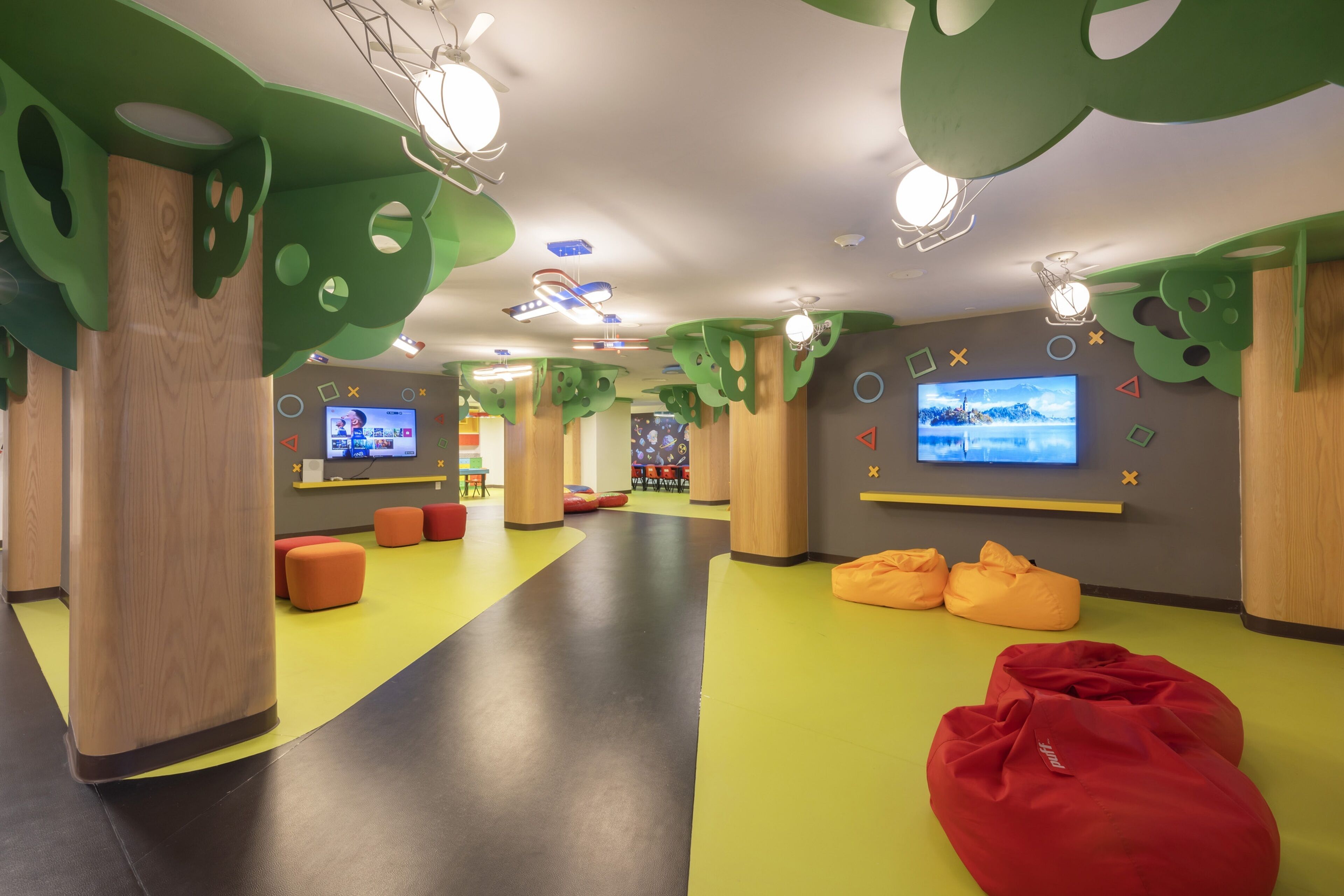 A children's play area with colorful flooring, bean bags, and a TV screen.