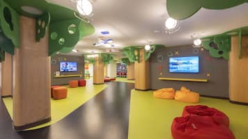 A children's play area with colorful flooring, bean bags, and a TV screen.