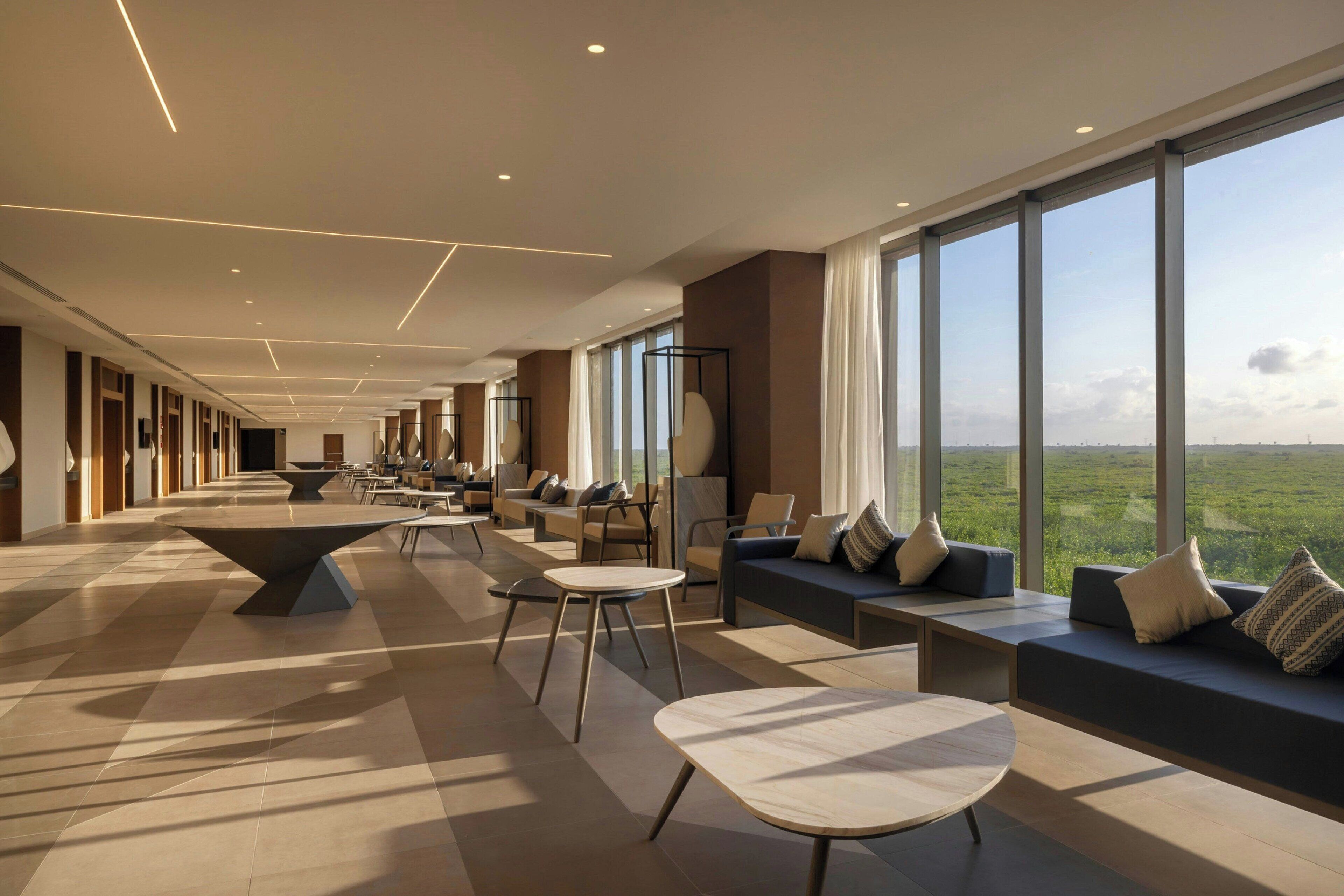 Un vaste espace intérieur doté d’une longue table, de différents types de sièges et de grandes fenêtres offrant une vue sur l’extérieur.