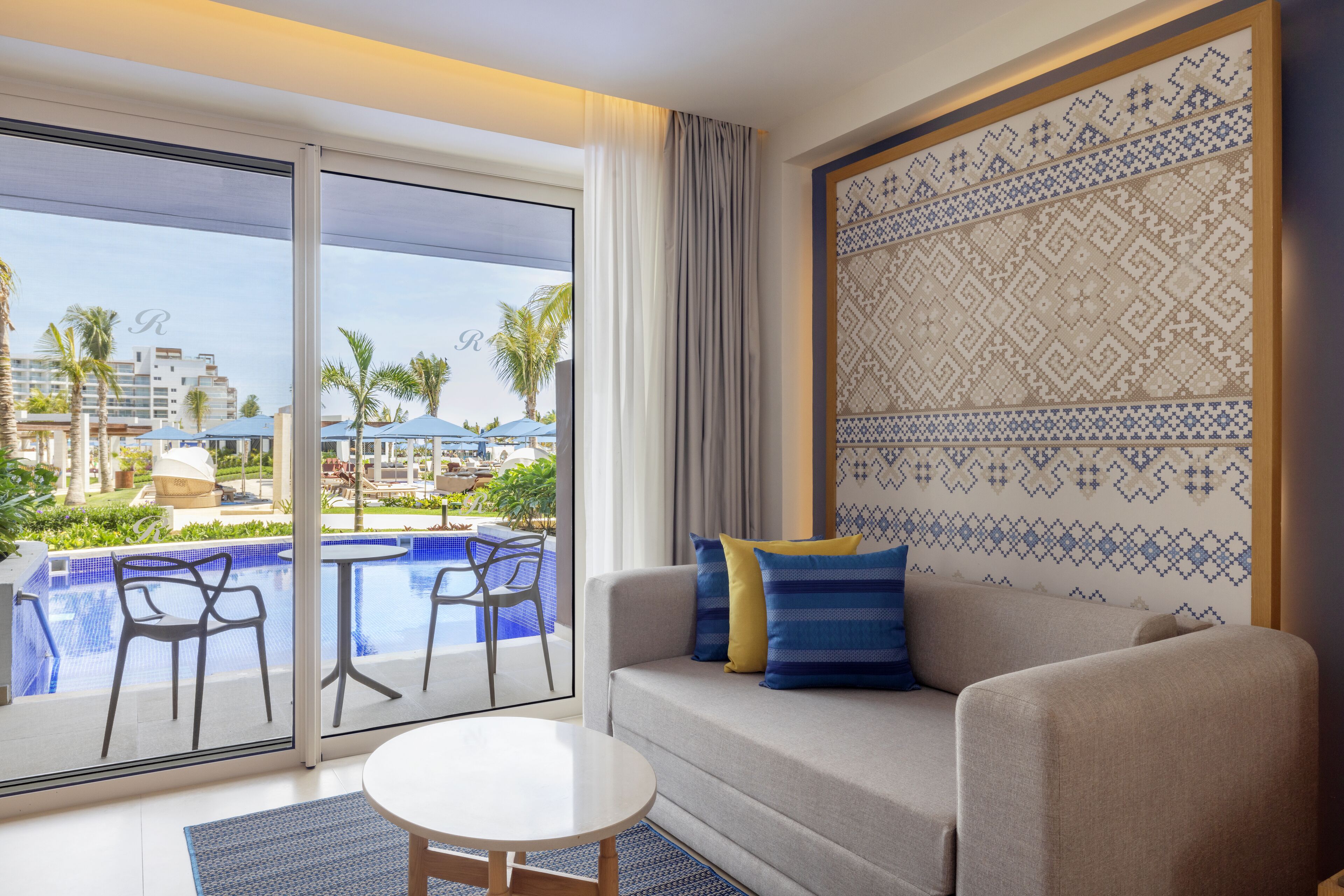 A hotel room with a balcony, a pool, and a view of palm trees and buildings.