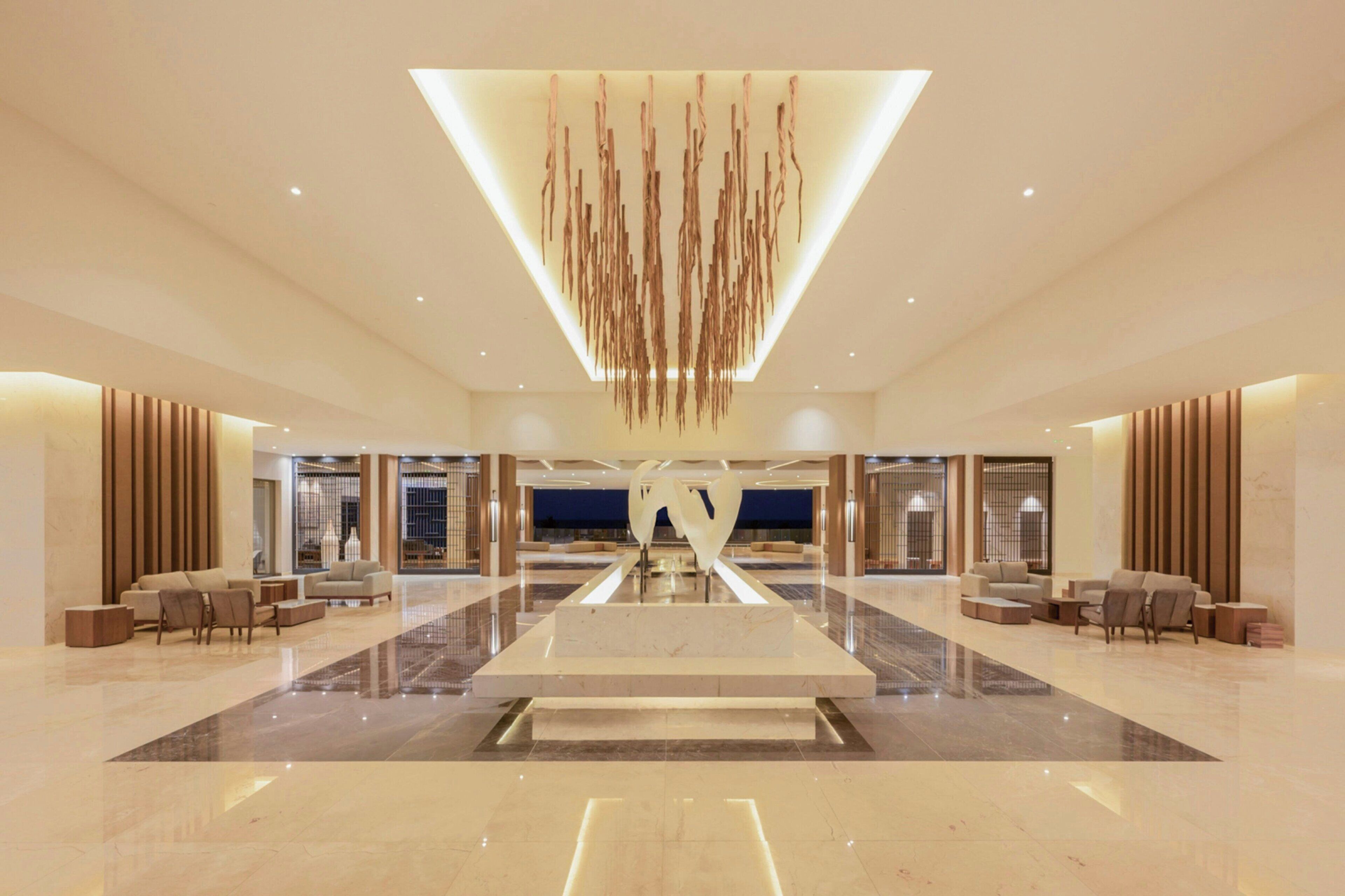 A spacious lobby with a central seating area, a modern chandelier, and a reflective floor.