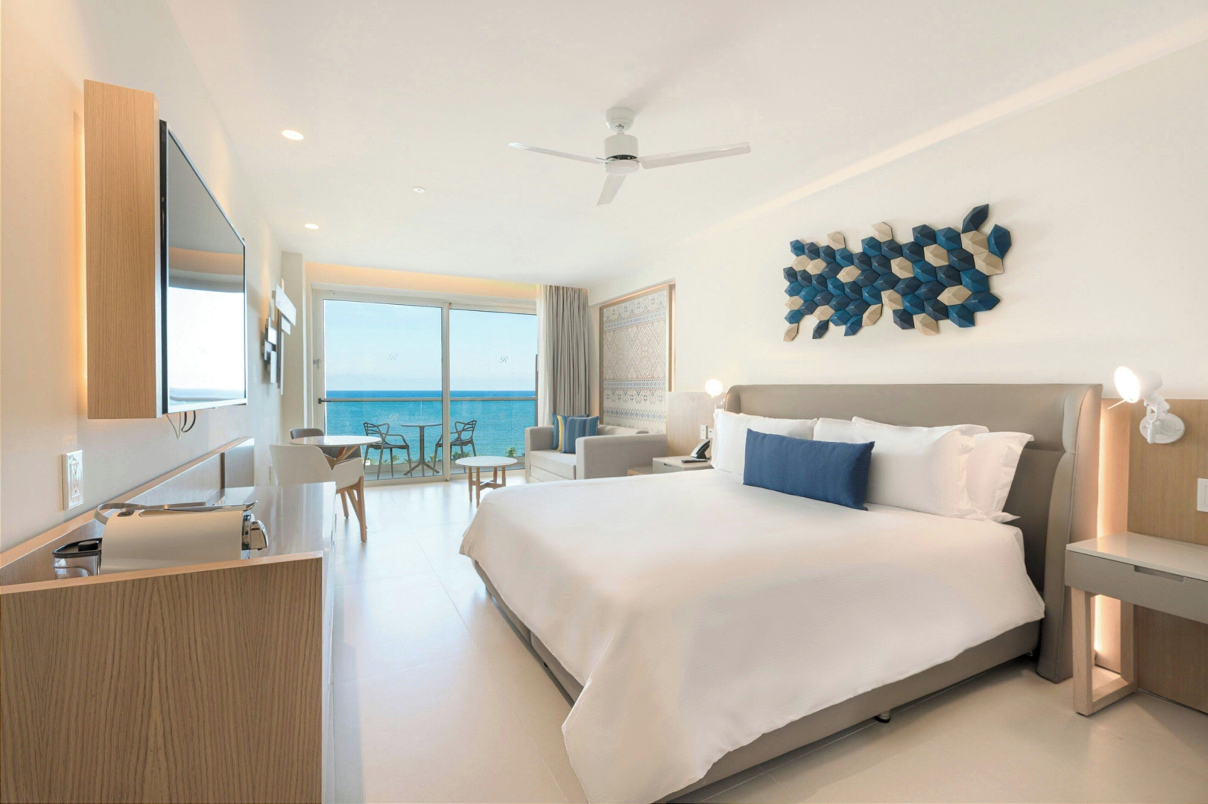 A modern hotel room with a large bed, a desk, and a view of the ocean.