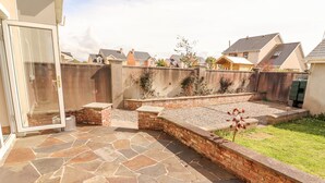 Un patio con piso de piedra, muros de ladrillo y una zona cubierta de césped.