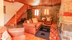 Una sala de estar acogedora con una escalera de madera, paredes de piedra y una chimenea.