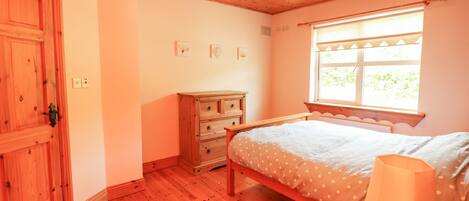 Ein Schlafzimmer mit Holzboden, einem Bett mit Punktenmuster-Bettdecke, einer Holzkommode und einem Fenster mit Jalousien.