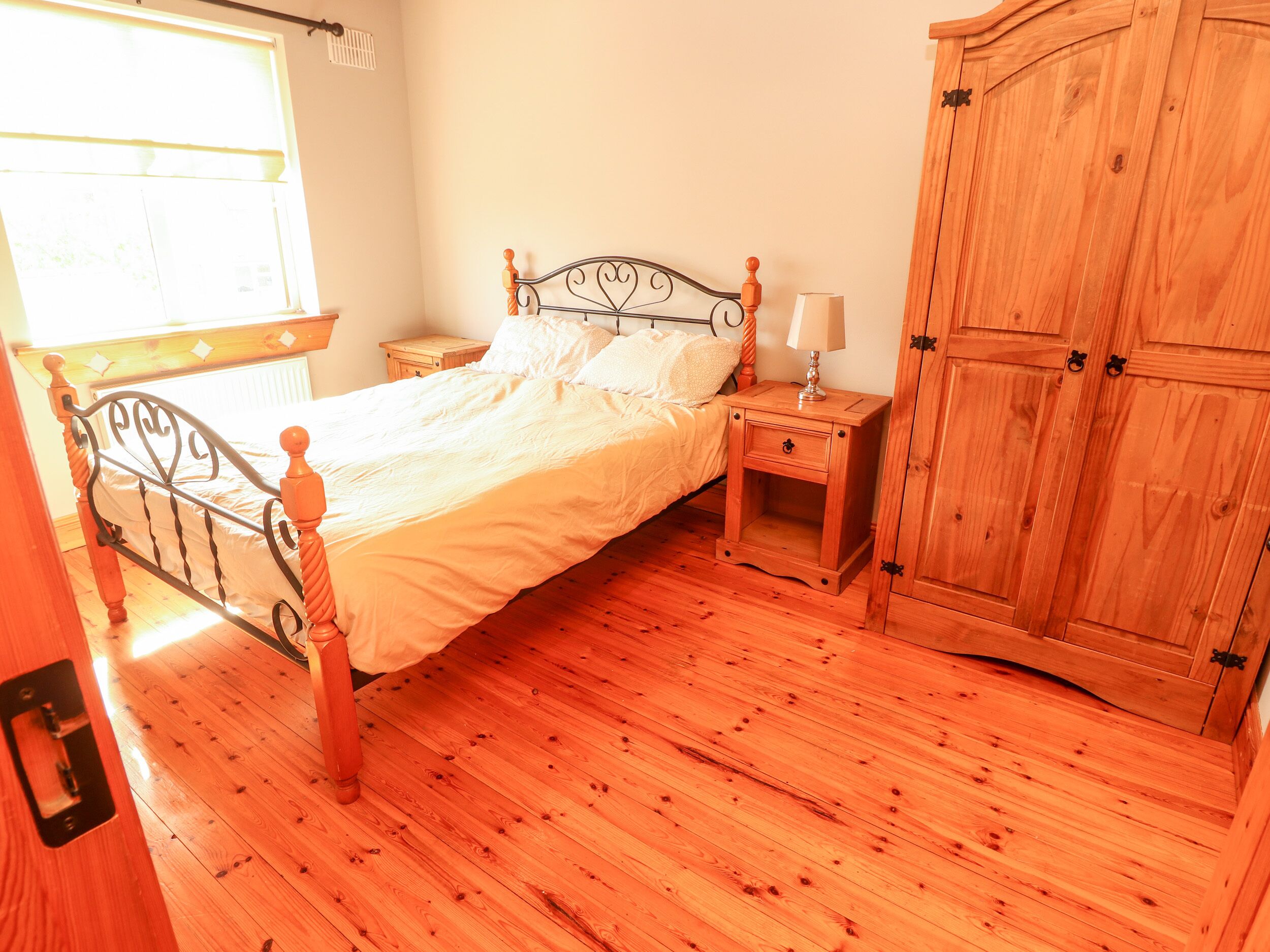 Un dormitorio con estructura de cama de madera, una mesita de noche, un armario de madera y una ventana con persianas.