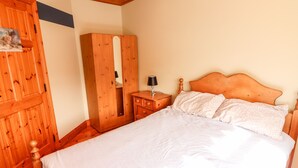 A bedroom with a wooden bed, a wooden wardrobe, and a nightstand with a lamp.