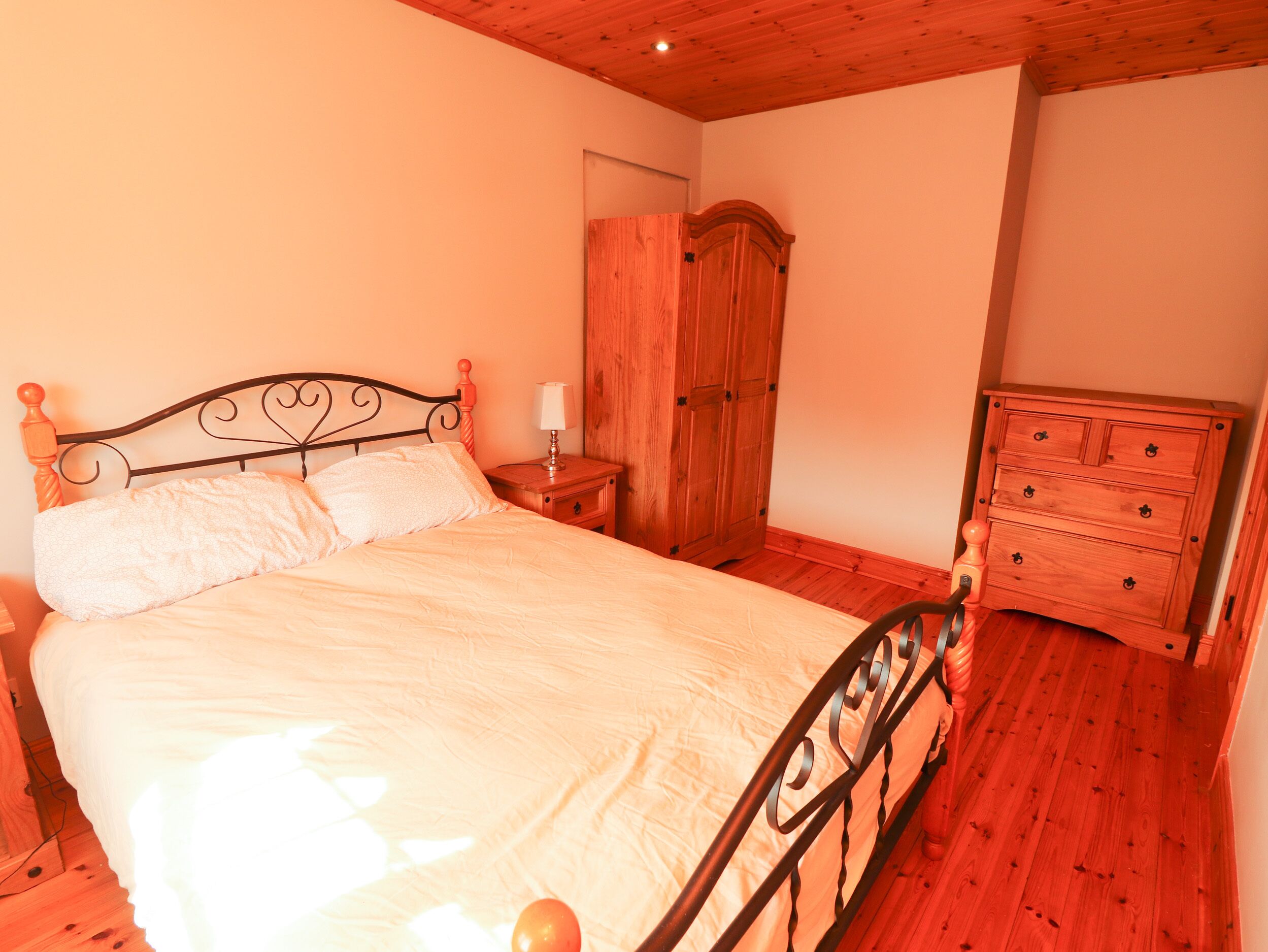 A bedroom with a wooden bed frame, a wooden wardrobe, and a dresser.