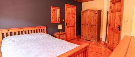A bedroom with a wooden bed, a nightstand, a mirror, and wooden wardrobes.